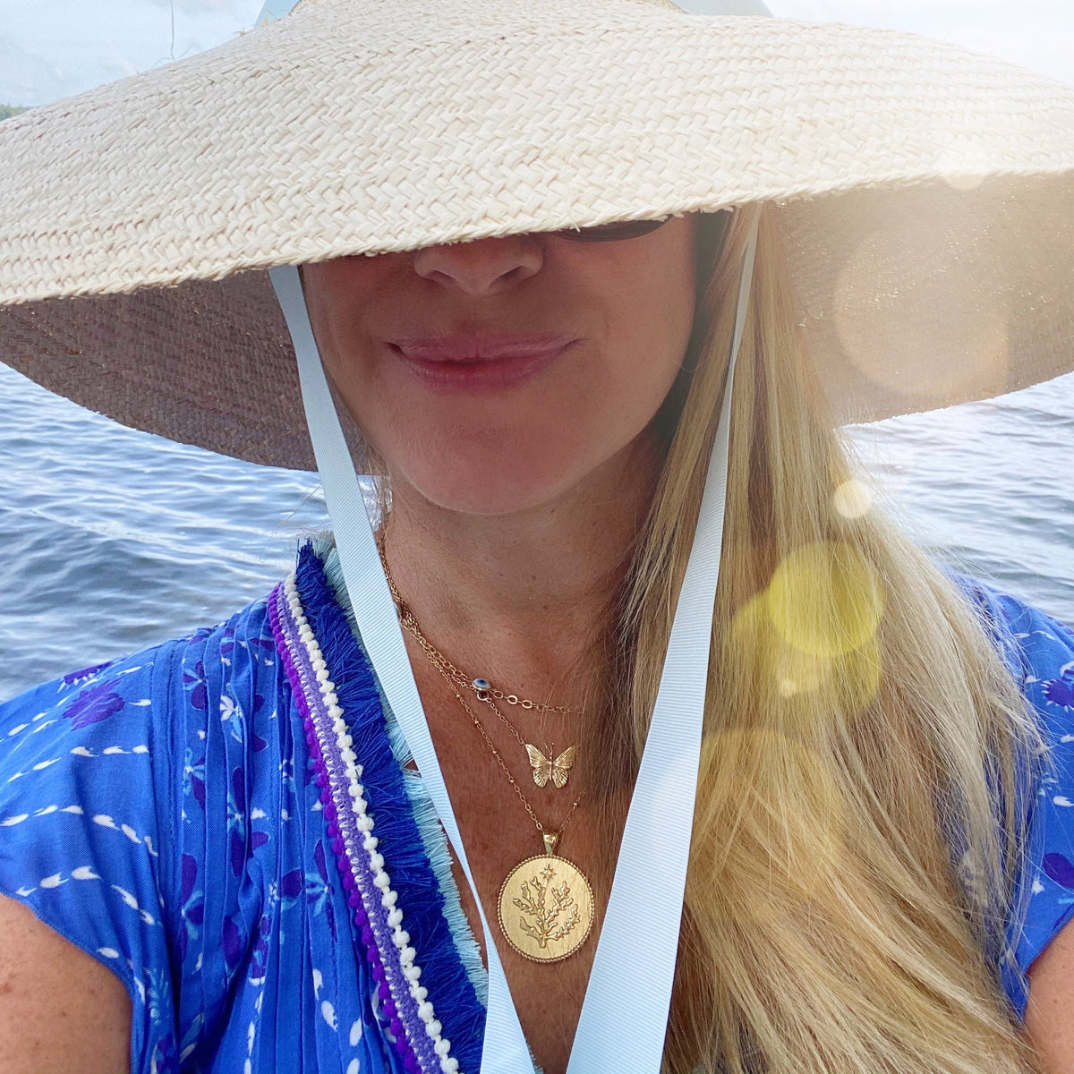 Close-up of Bermuda JW Original Pendant Coin Necklace showcasing coral design on a model with an ocean background