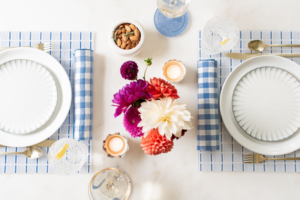 Styled table with Stewart blue check placemats, matching napkins, white plates, gold flatware, and a small floral centerpiece