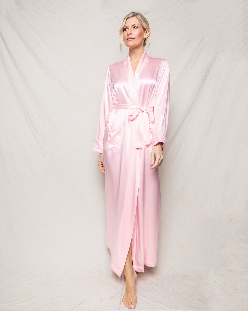 Front view of women’s pink silk long robe showcasing ankle-length cut, tie waist and front pockets on light fabric backdrop