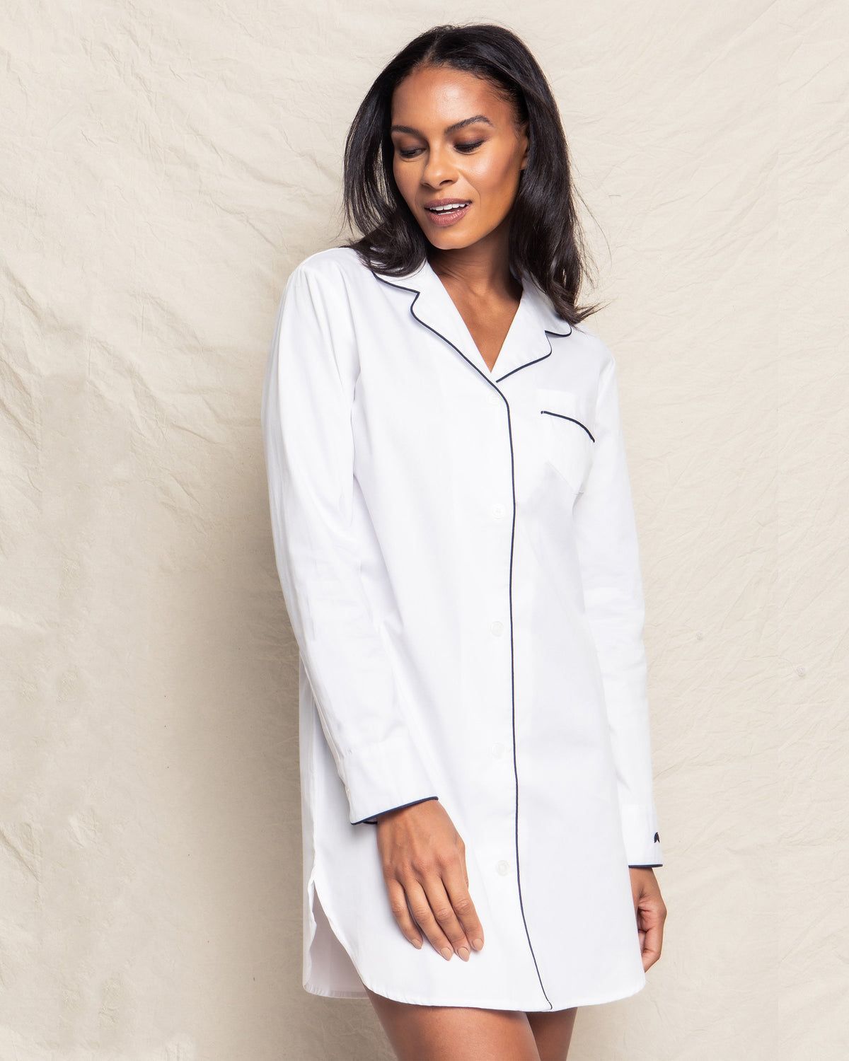 Three quarter view of women’s white nightshirt on model showing navy piping on collar and pocket, long sleeves, mid-thigh