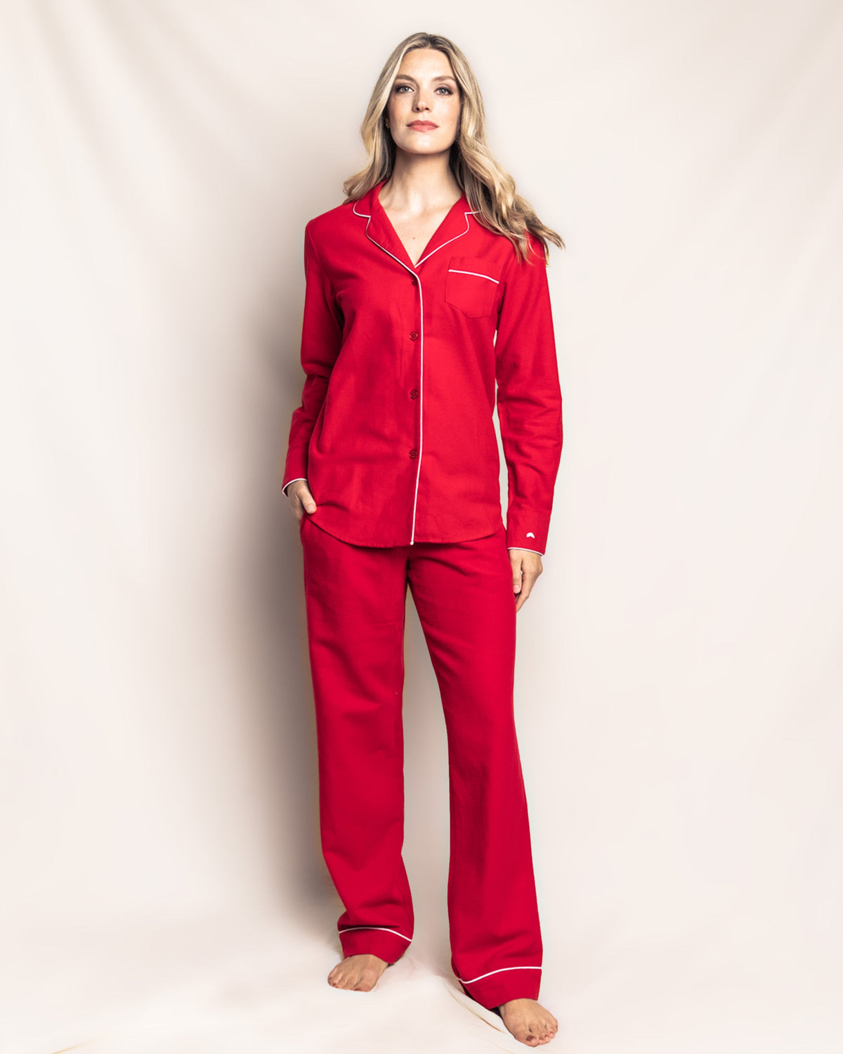 Front view of women’s red flannel pajama set with white contrast piping, button-front top and relaxed straight-leg pants on model