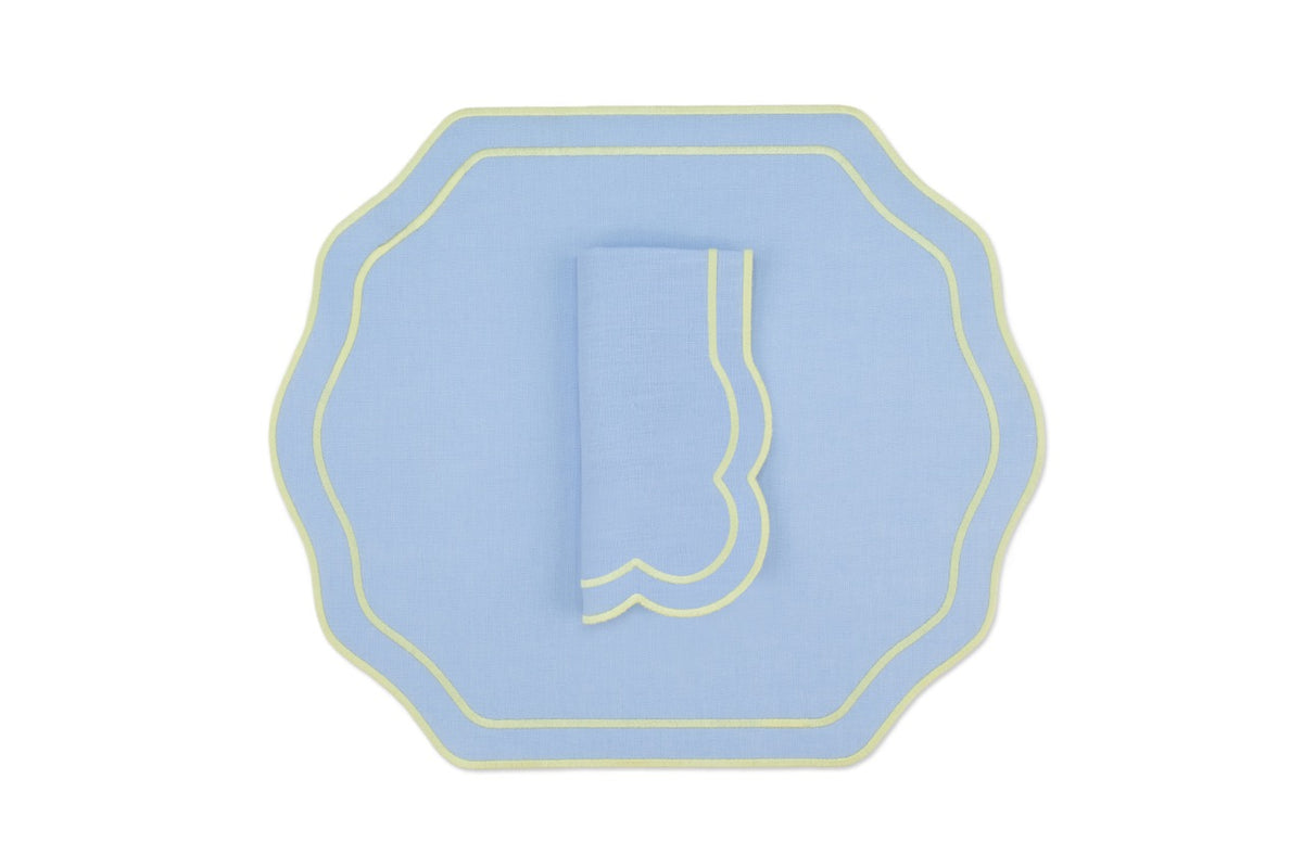 Top-down view of Stucco linen placemat and folded napkin in air blue with yellow scalloped trim on white background