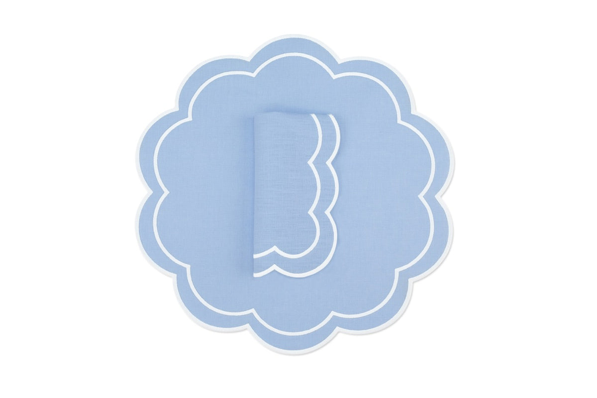 Top view of Bloom linen napkin and scalloped placemat set of 4 in air blue with white double-stitching on white background