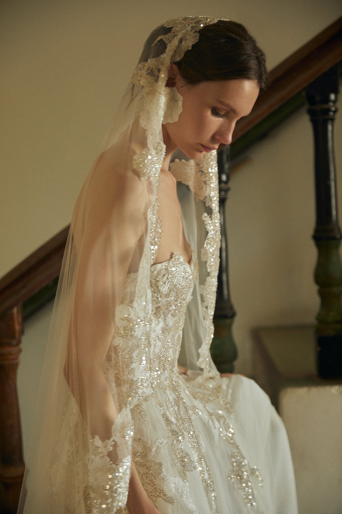 Side view of Amaranta veil on model showing mid-length tulle with embroidered appliques and sequin trim against staircase