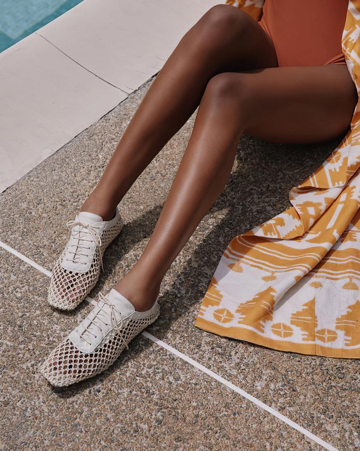 Angled top-down view of Antonia flat showing woven net upper and lace-up front on a poolside tiled surface