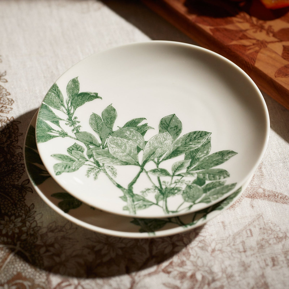 Close-up view of Arbor Green Canapé Plate showcasing leafy green branches on creamy white porcelain with a patterned tablecloth background