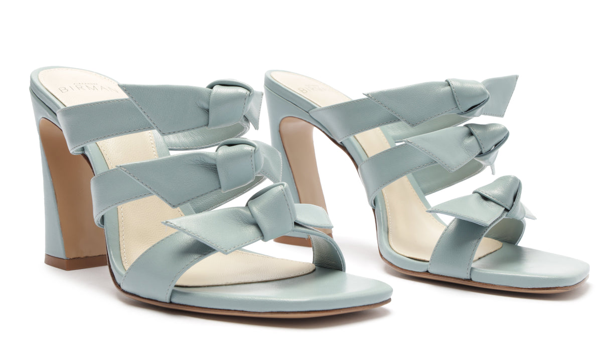 Three-quarter view of Lolita Square 90 Nappa Leather Sandal showcasing pale blue-gray bow straps and block heel on white background