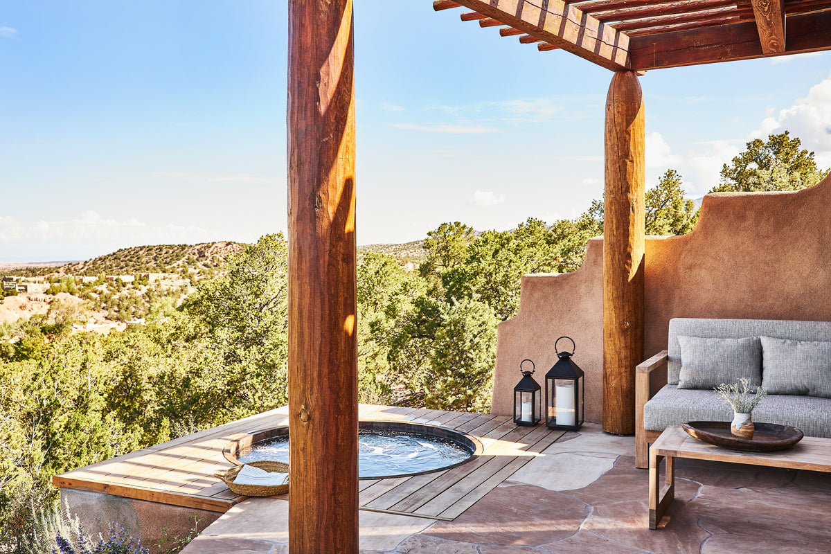 Adobe-style patio with wooden pergola, round plunge pool, cushioned sofa and lanterns overlooking juniper-covered desert hills