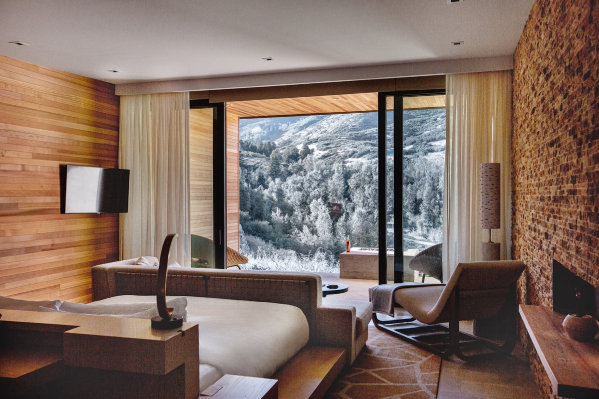 Spacious hotel suite with king bed and seating area opening to a snowy mountain view through floor to ceiling glass doors