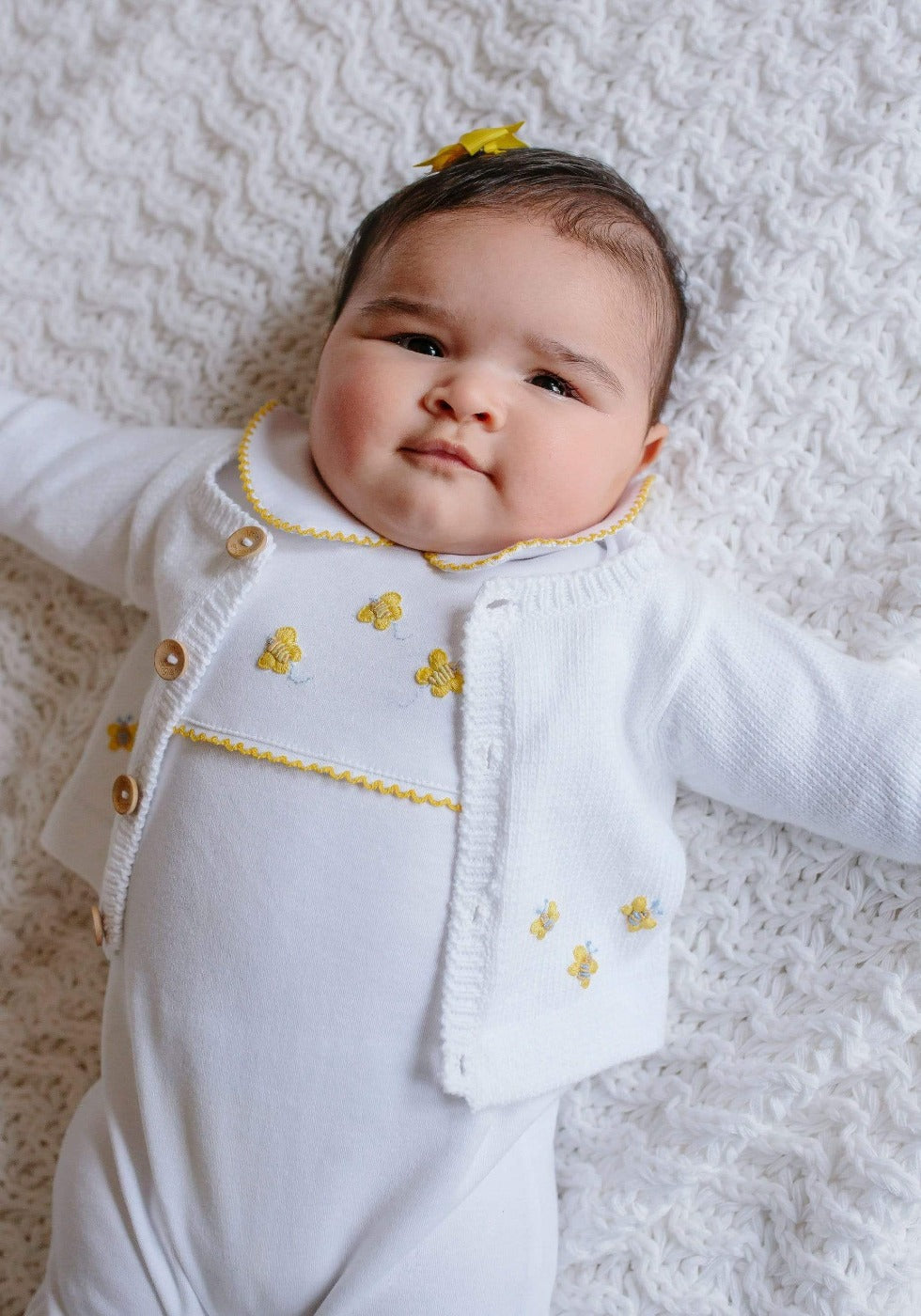 Top view of baby in white Bee Crochet Playsuit with yellow bee embroidery and Peter Pan collar on white knit blanket