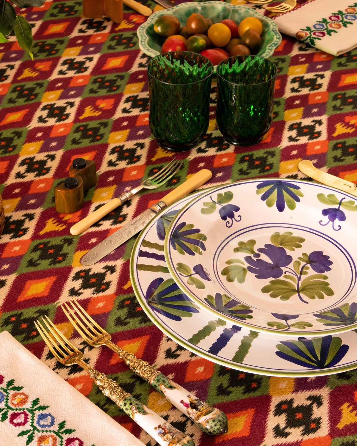 Angled view of Blossom soup plate in blue showing hand-painted blue and green floral motif on white ceramic, set on a colorful patterned tablecloth