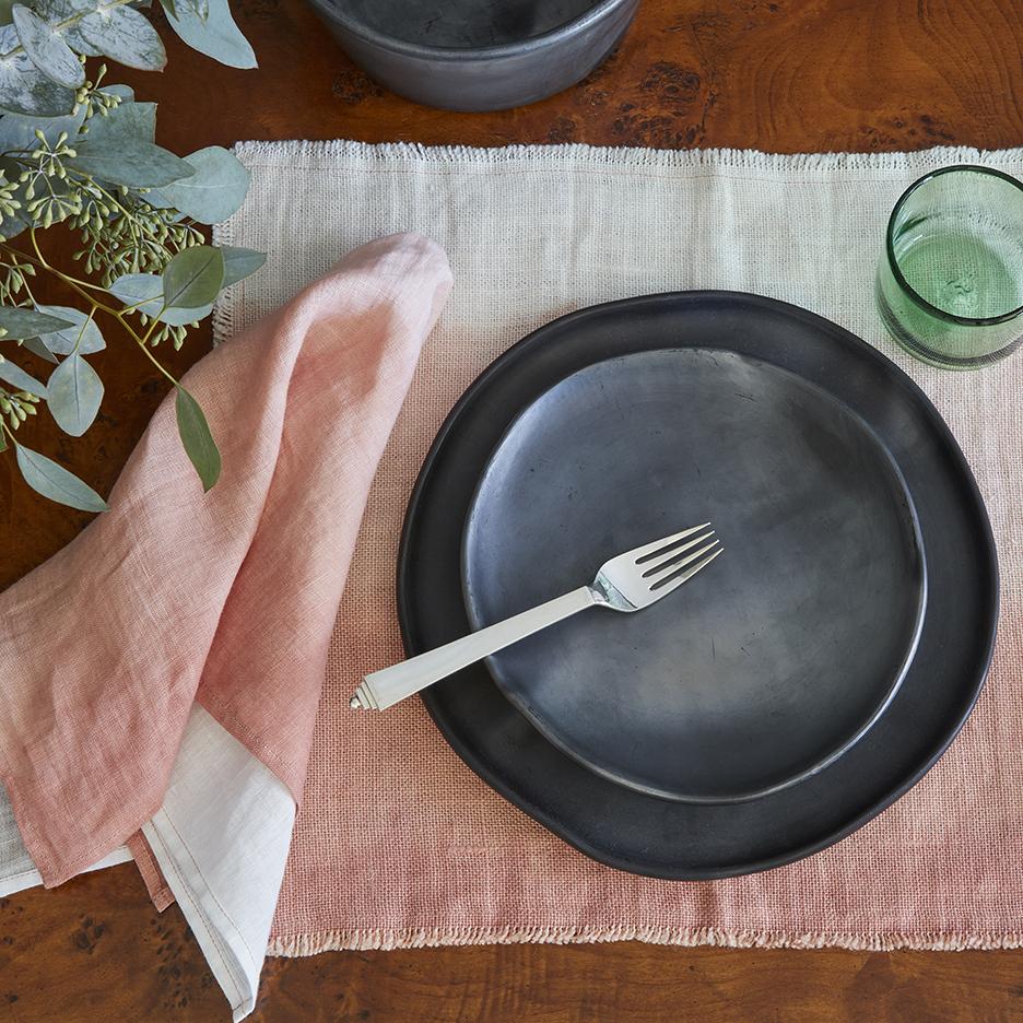 Overhead view of Blush Linen Napkin showcasing hand dyed linen on a table setting with black plates and glassware