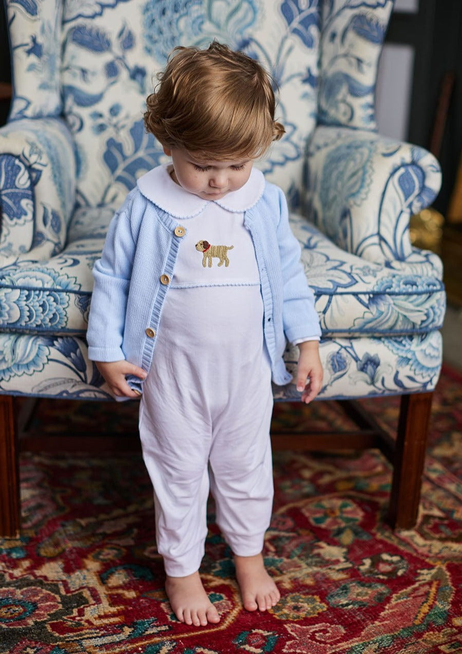 Front view of Boy Lab crochet sweater on toddler showing light blue knit, dog motif and wooden buttons, patterned armchair