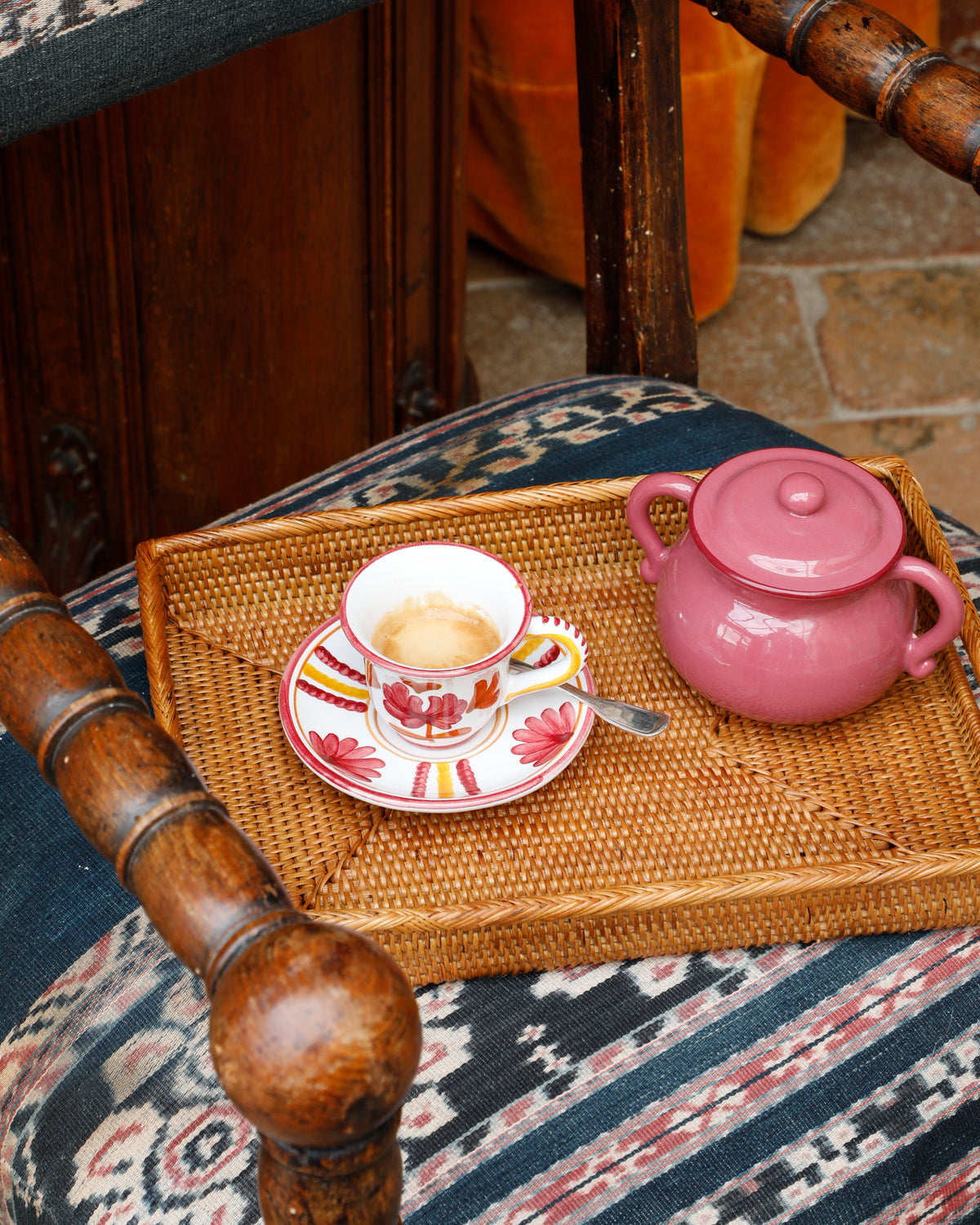Pink ceramic Britwell sugar pot with lid beside a floral espresso cup on a woven tray on a patterned wooden chair