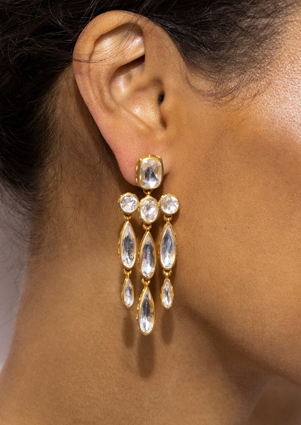 Close up of Catherine Long Girandole earrings in white gold wash showcasing teardrop crystal drops on a model’s ear