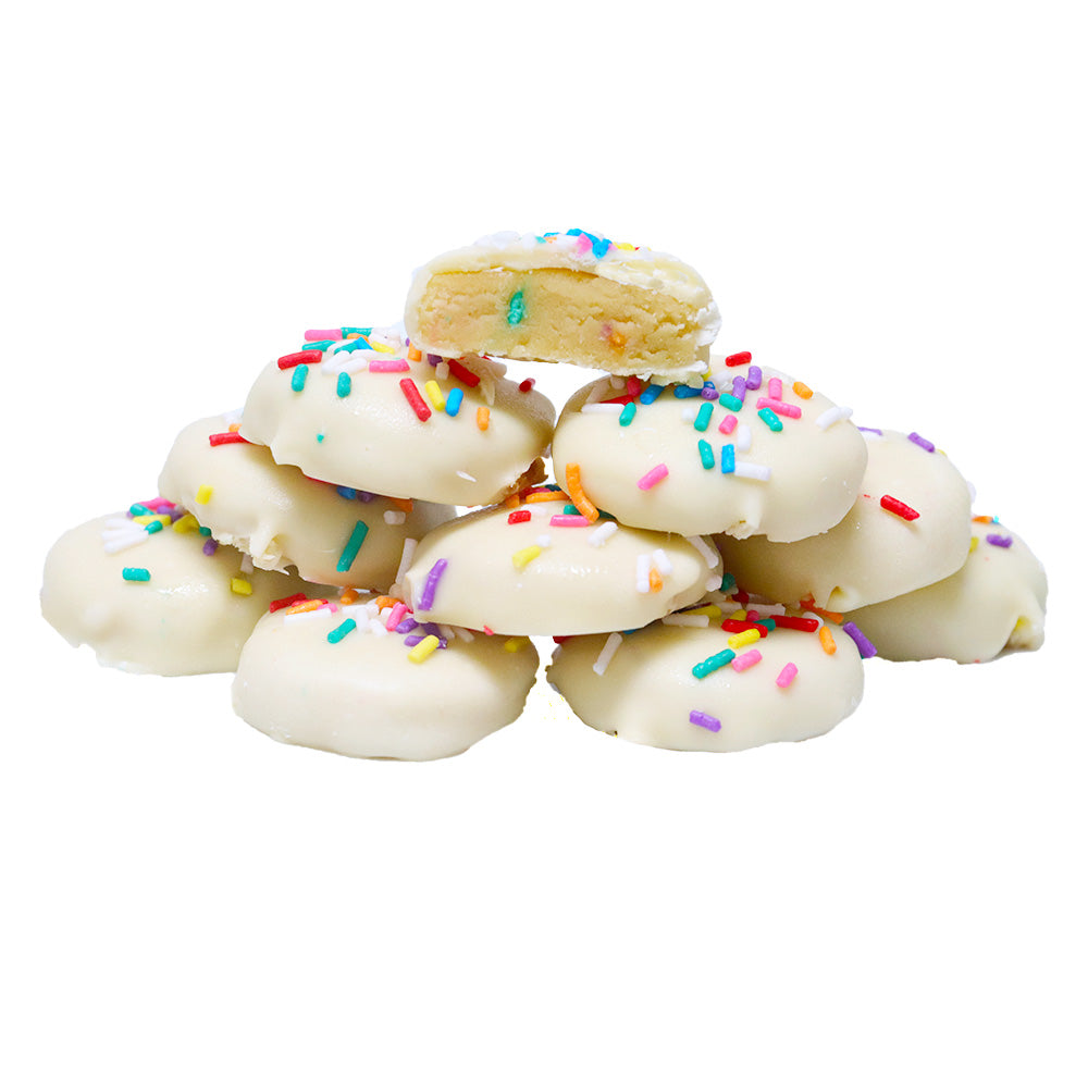 Pile of Birthday Cake Bites with white chocolate coating, rainbow sprinkles, and one cut to reveal yellow cake on white