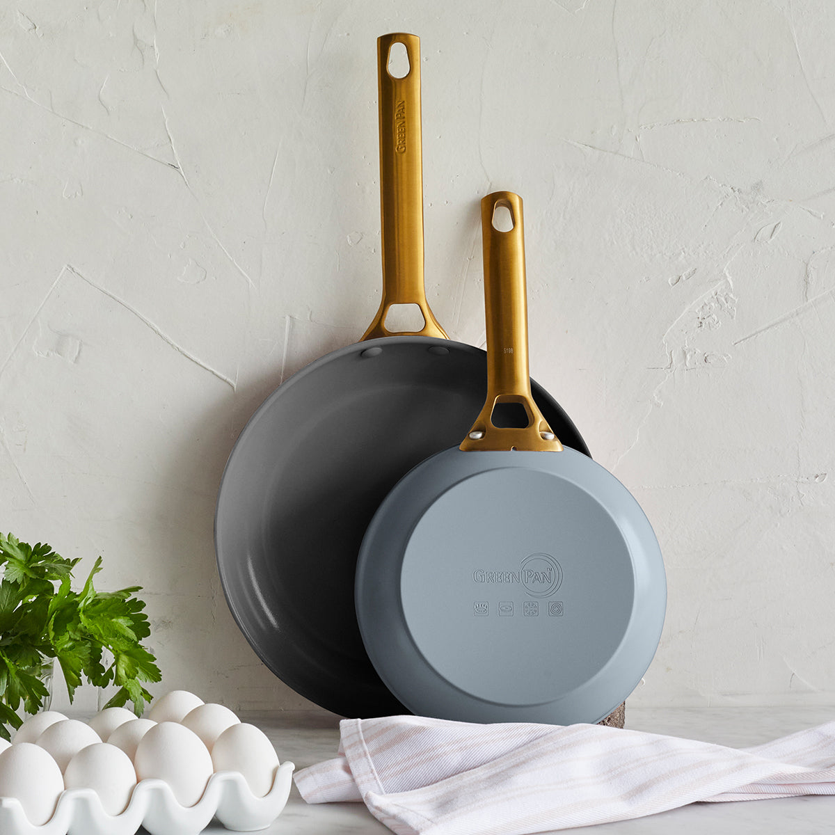 Front view of Reserve Collection Fry Pan 2-Piece Set in Charcoal showcasing two pans with gold handles against a white wall
