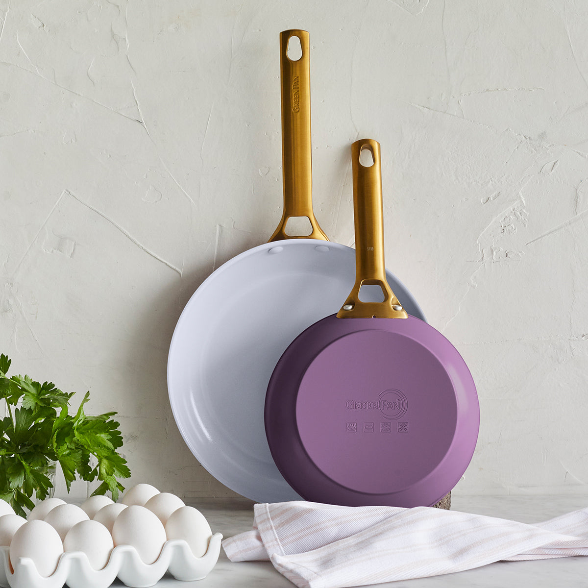 Angled view of Reserve Collection 2-Piece Fry Pan Set in Eggplant with gold handles against a textured wall