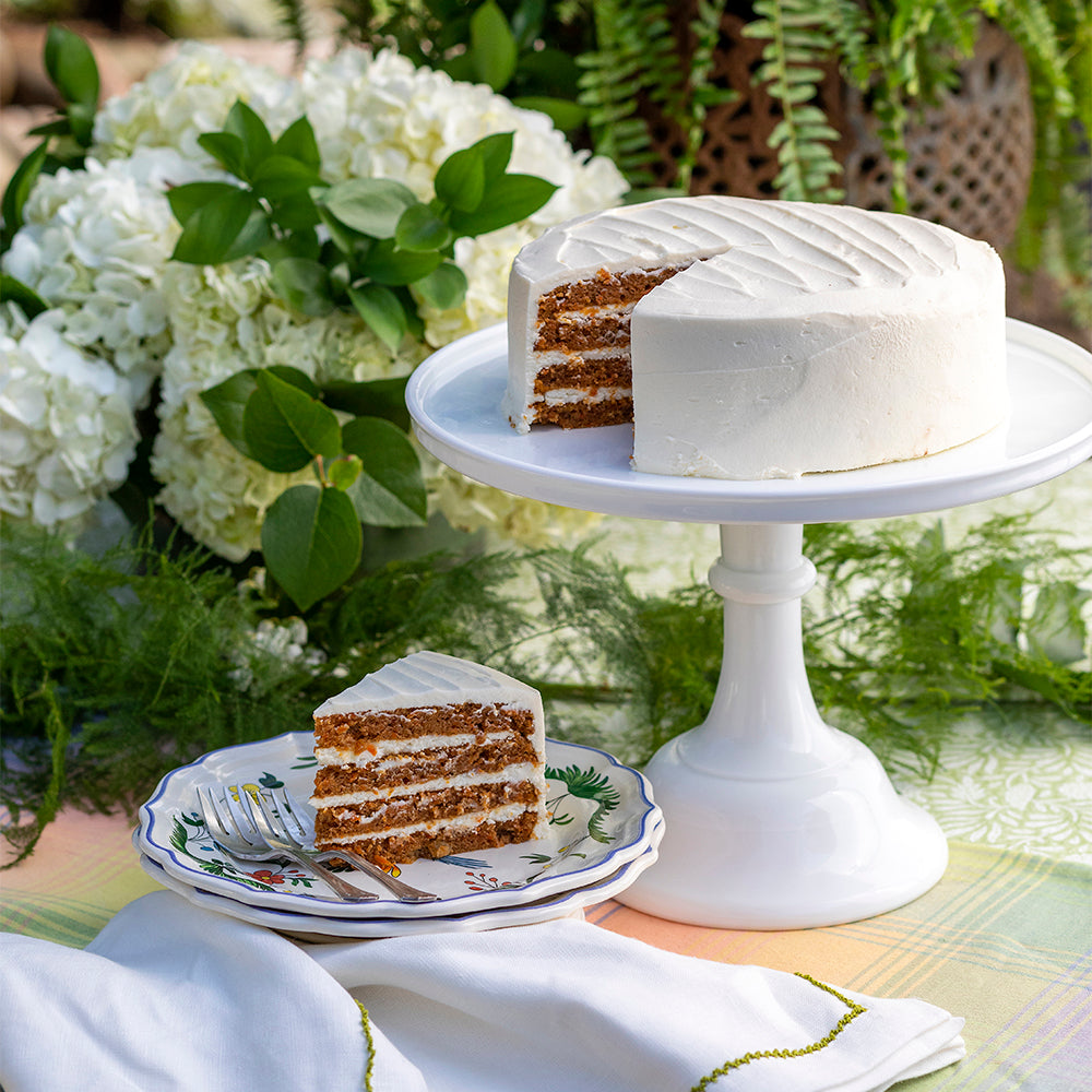 Angled view of Traditional Carrot Cake with four cream cheese filled layers and a slice on a white cake stand