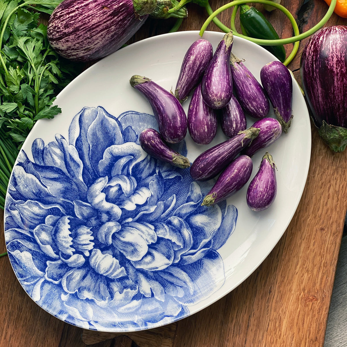 A Peony Blue Medium Coupe Oval Platter from Caskata Artisanal Home adorned with deliciously roasted eggplants.