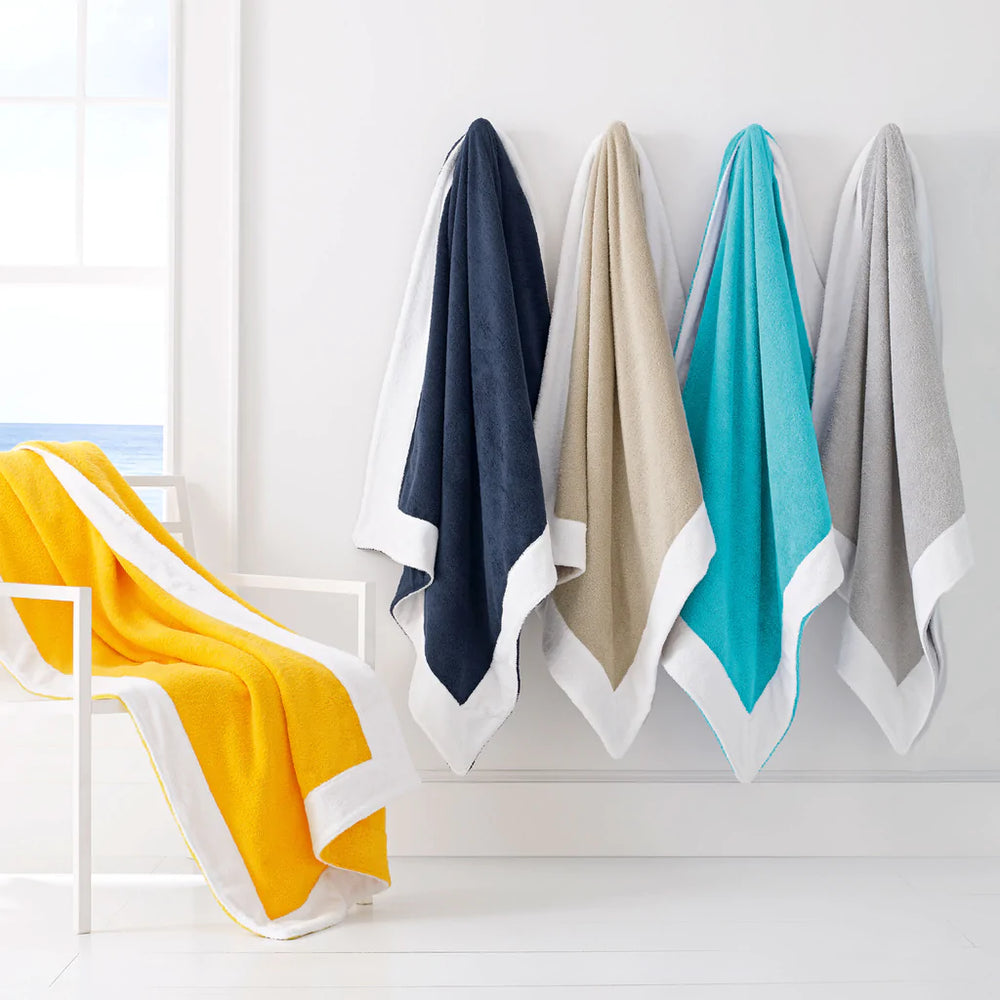Hanging Capri beach towels with white hem in yellow, navy, dune, aqua, and gray on a white wall