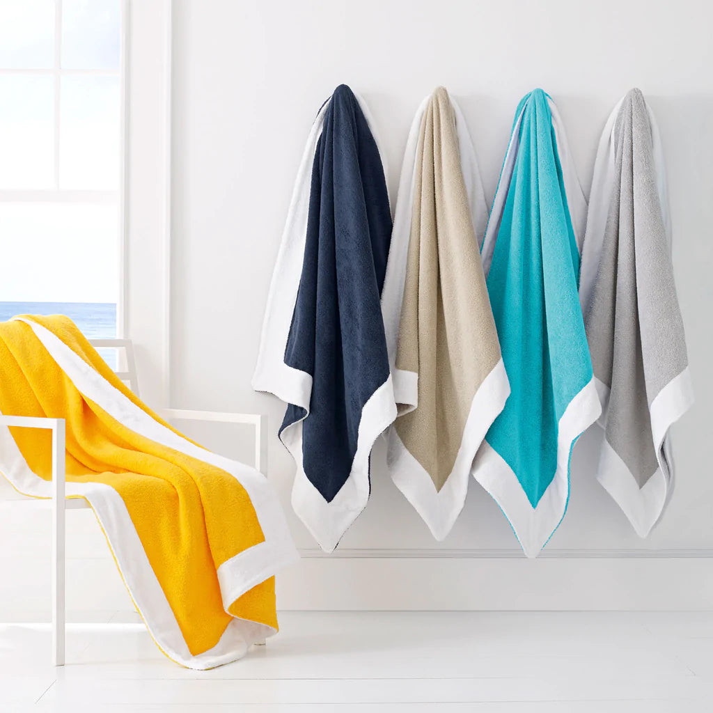 Hanging Capri beach towels with white hem in yellow, navy, dune, aqua, and gray on a white wall