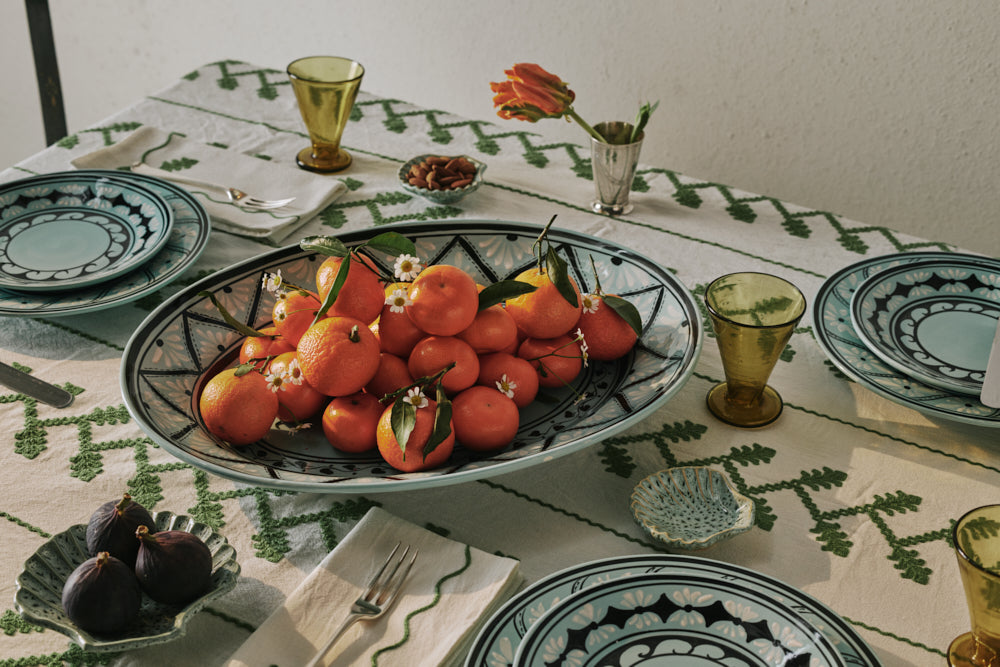 Aqua oval platter filled with oranges on a table set with patterned plates and glasses