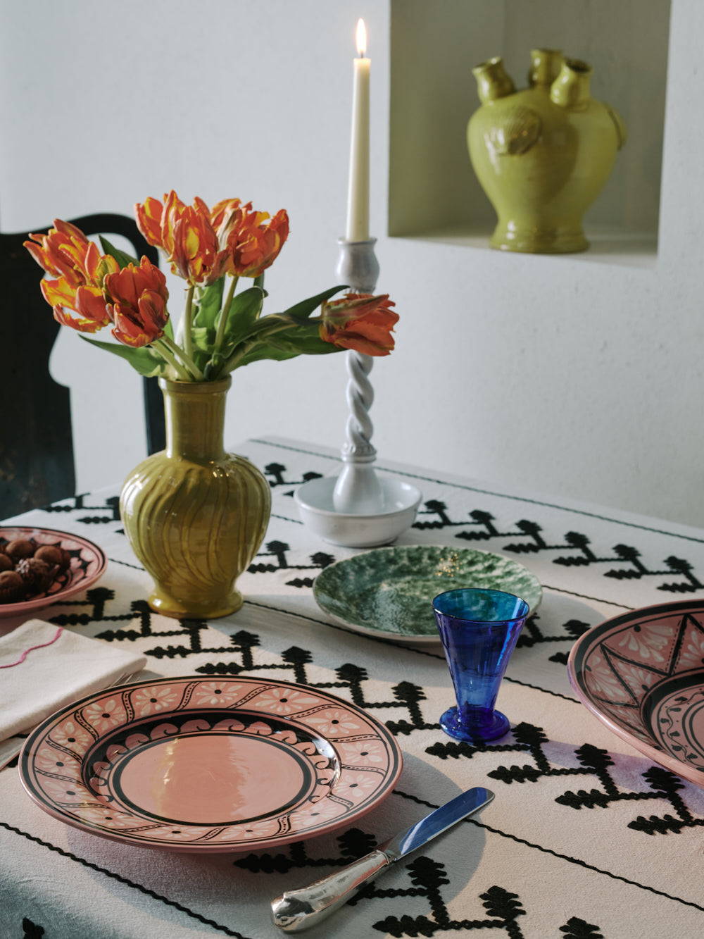 Angled top view of Gigi pink dessert plate showcasing hand-painted geometric and wave border on a patterned tablecloth