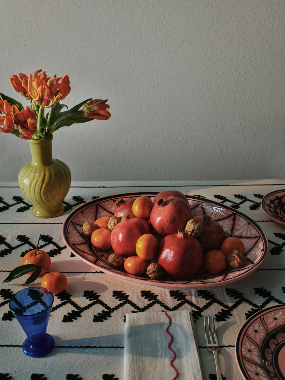 Angled view of Gigi Pink Oval Platter showcasing hand-painted geometric and wave patterns with fruit on a patterned table