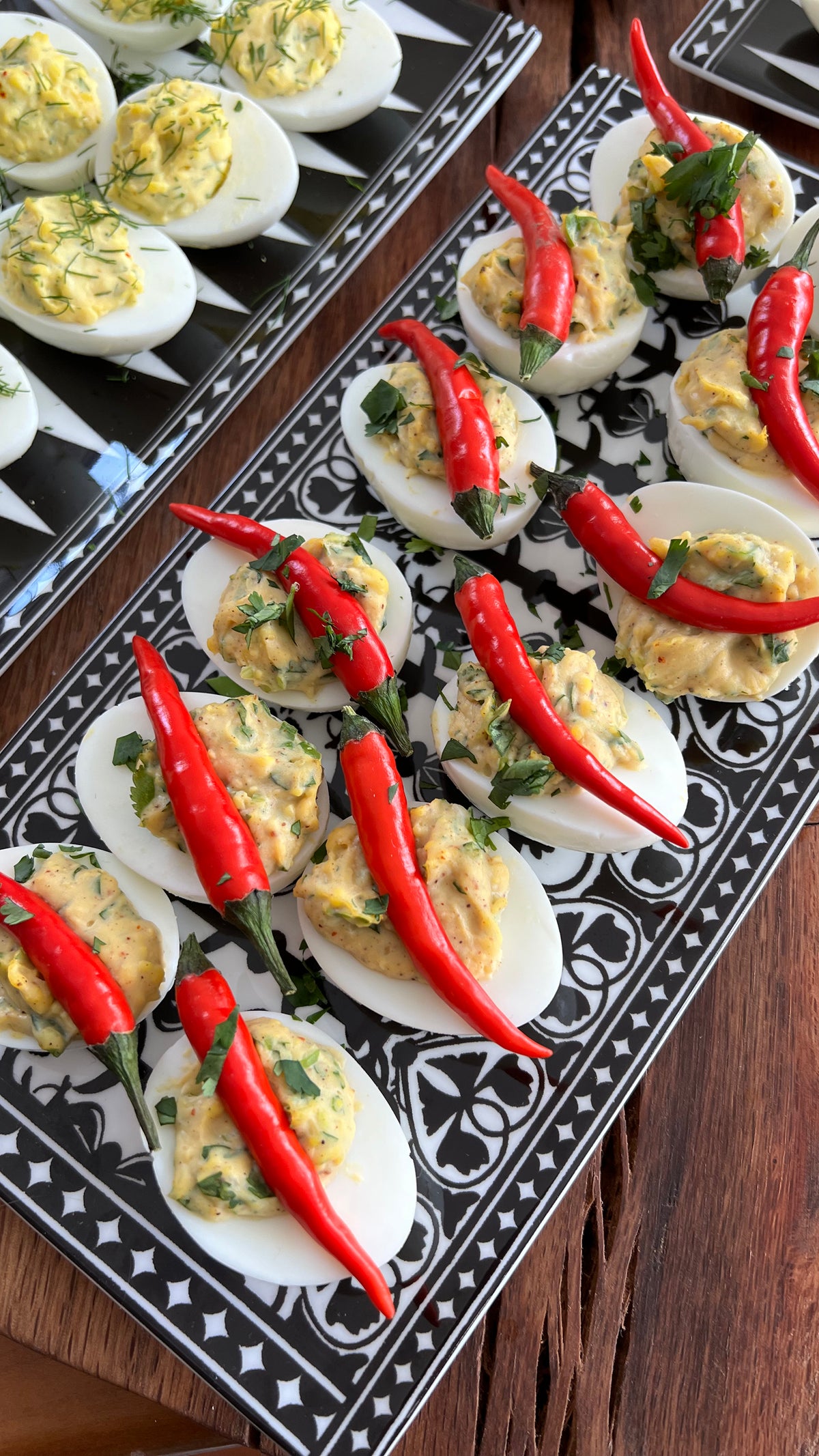 Deviled eggs arranged on black and white Casablanca sushi trays with red peppers on a wooden table
