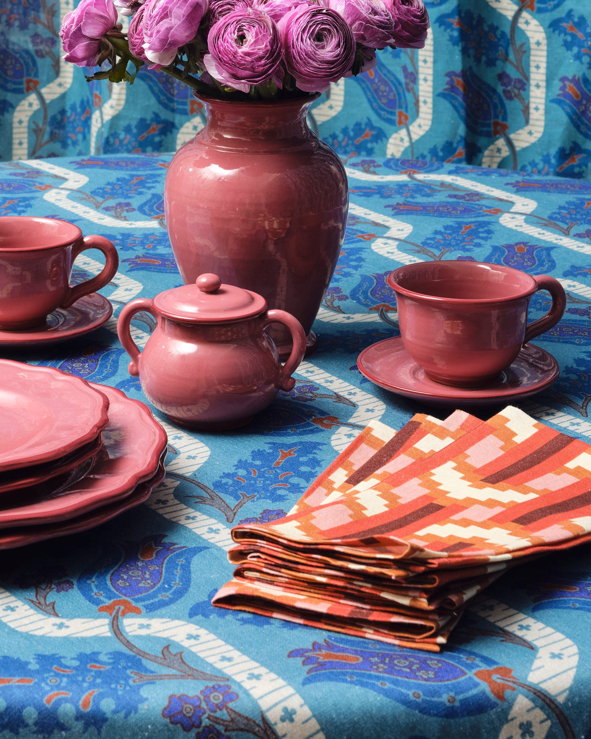 Chevron napkins arranged on a blue patterned tablecloth beside pink tableware and flowers