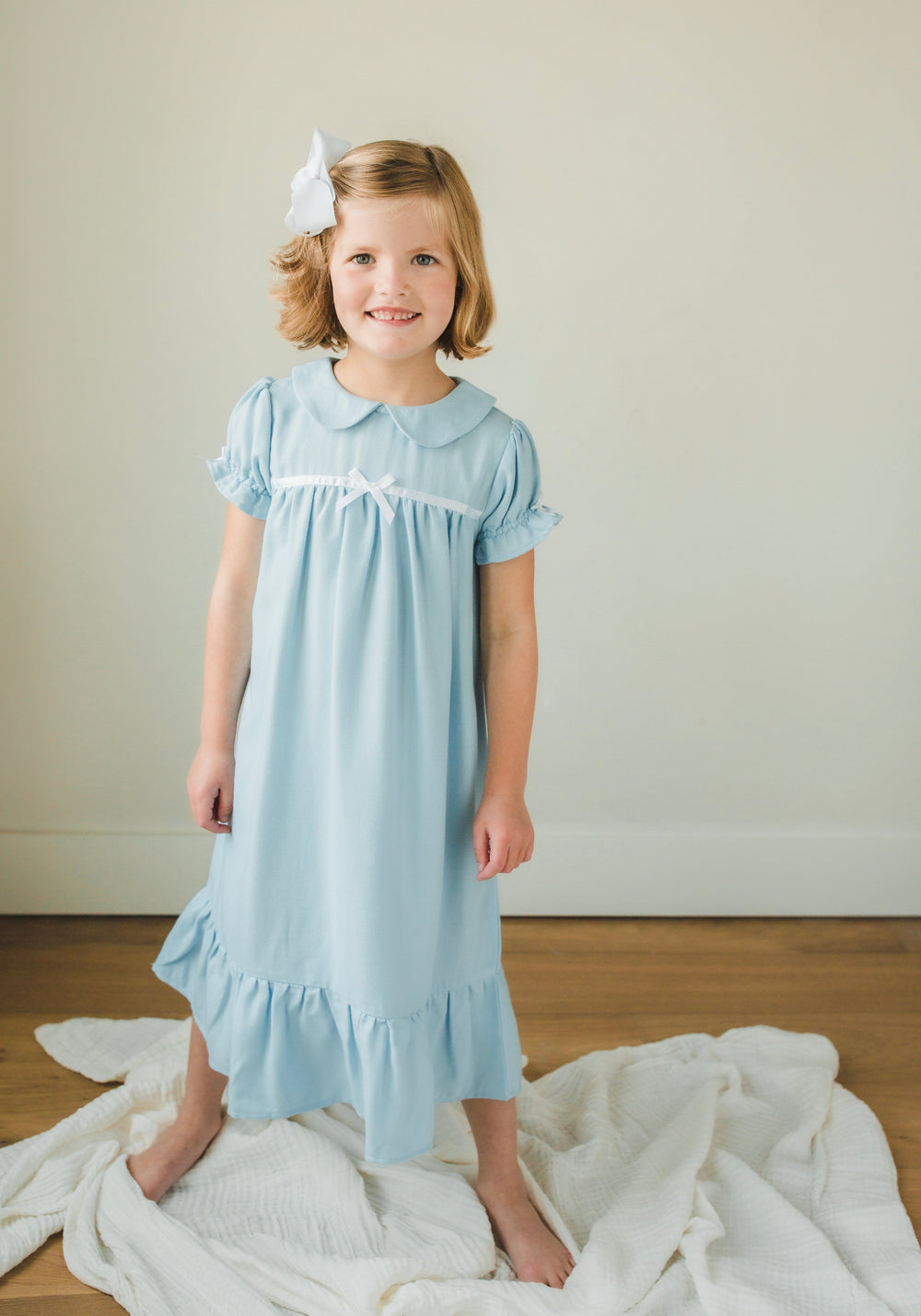 Front of classic short-sleeve girls’ nightgown in light blue with Peter Pan collar, small bow, puff sleeves and ruffled hem on model