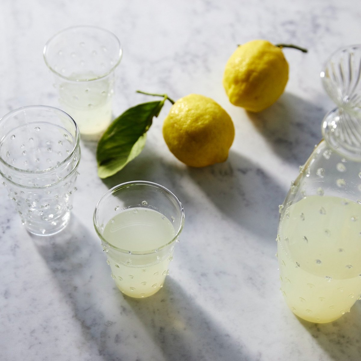 Overhead view of Clear Pom Water Glass showcasing its clear bobble design with lemons and lemonade on a marble surface