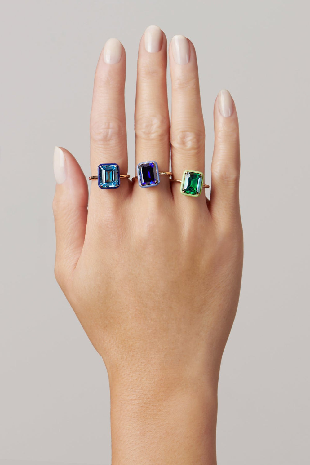 Hand wearing Rectangular Blue Topaz cocktail ring with rectangular blue topaz set in gold, flanked by two colored stones on gray background