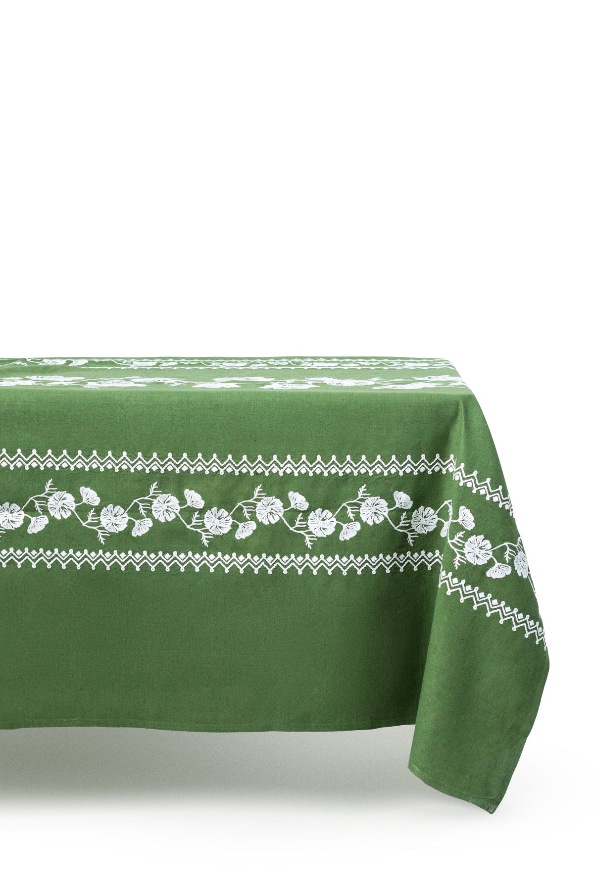 Angled view of Cosmo Rectangular Tablecloth in Green showcasing white floral embroidery and geometric border on a white background