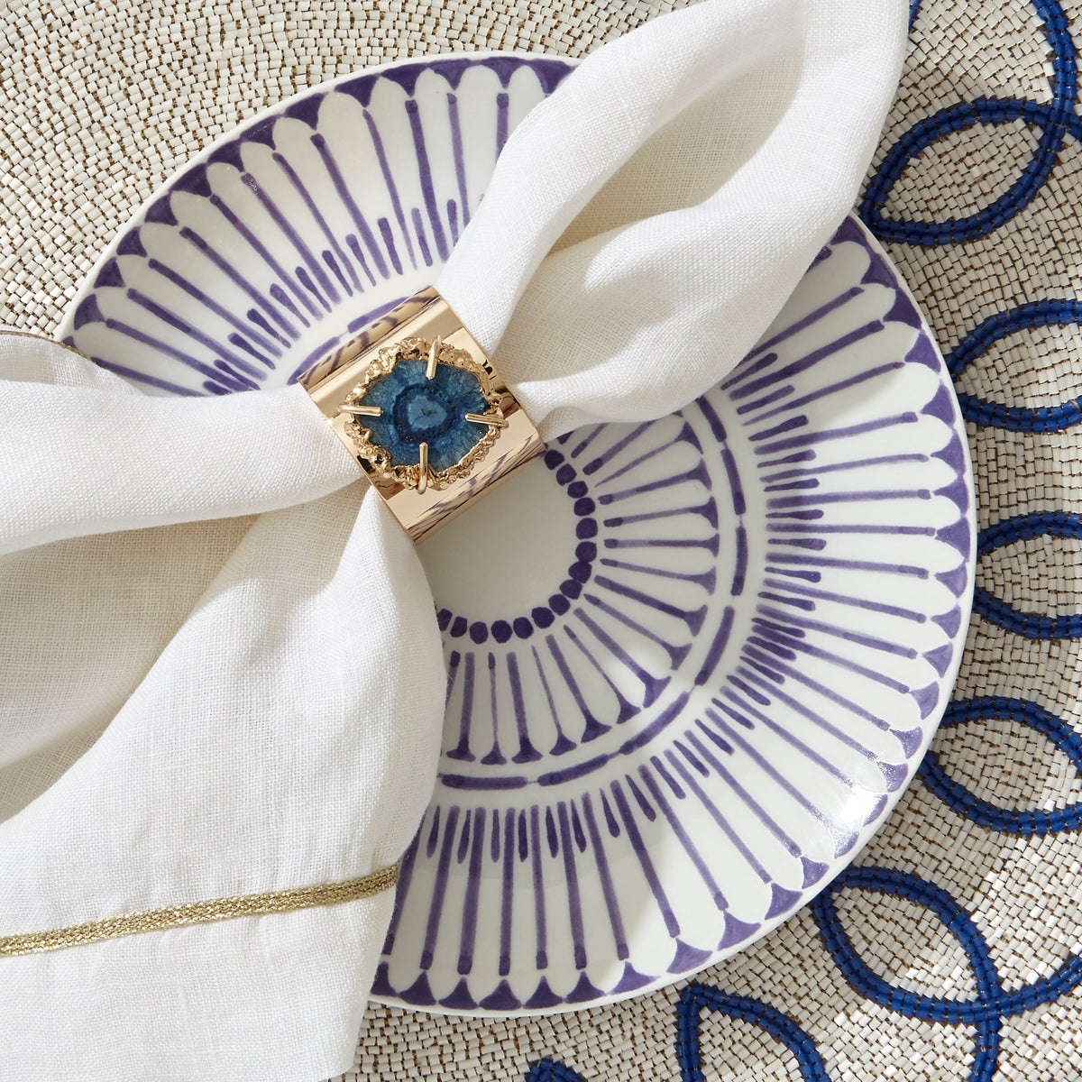 Close-up of Crystal Quartz Napkin Rings in Indigo, set of two, showcasing blue quartz and gold finish on a white napkin