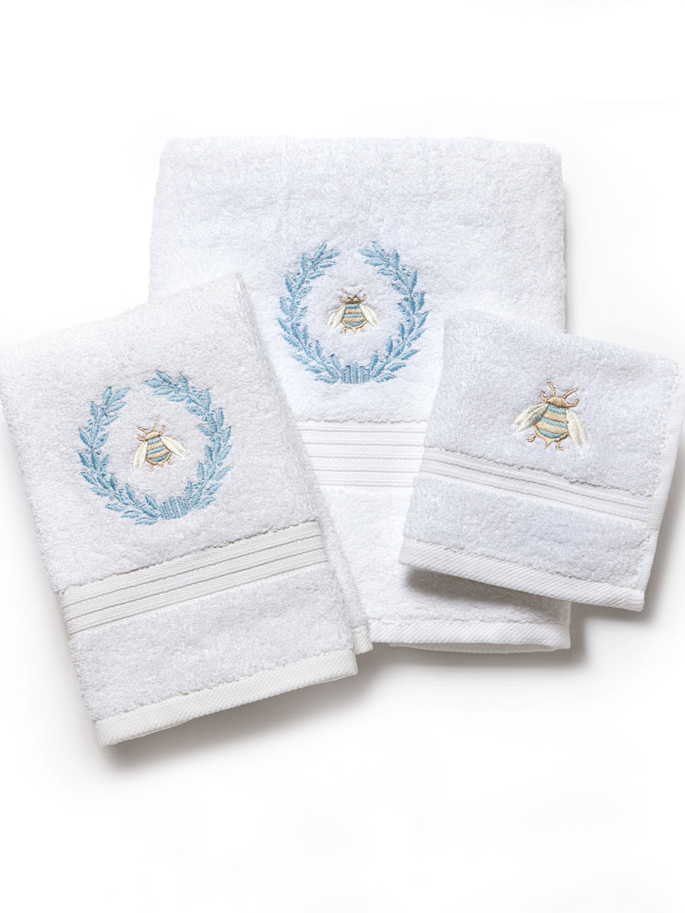 Flat lay of three white terry towels showcasing blue embroidered bee and laurel wreath accents on a white background