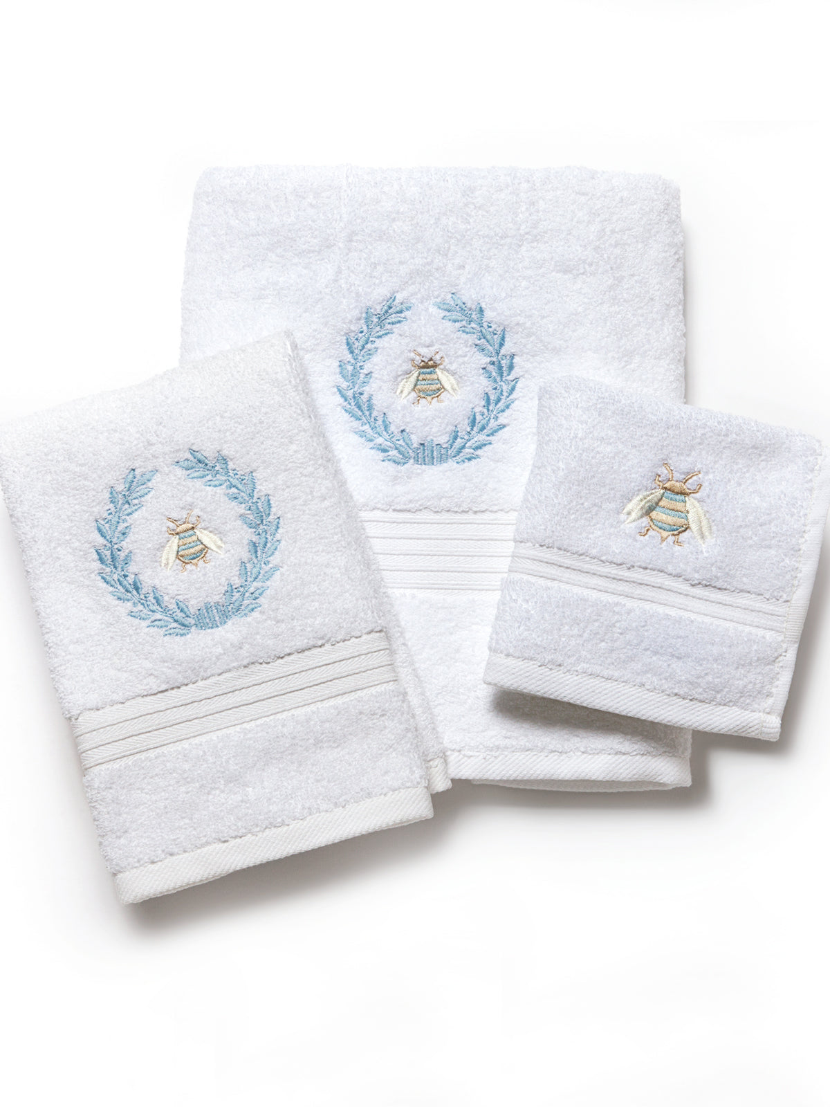 Flat lay of three white terry towels showcasing blue embroidered bee and laurel wreath accents on a white background