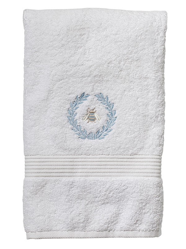 Front view of terry bath towel showcasing blue embroidered Napoleon bee wreath and ribbed band on white background