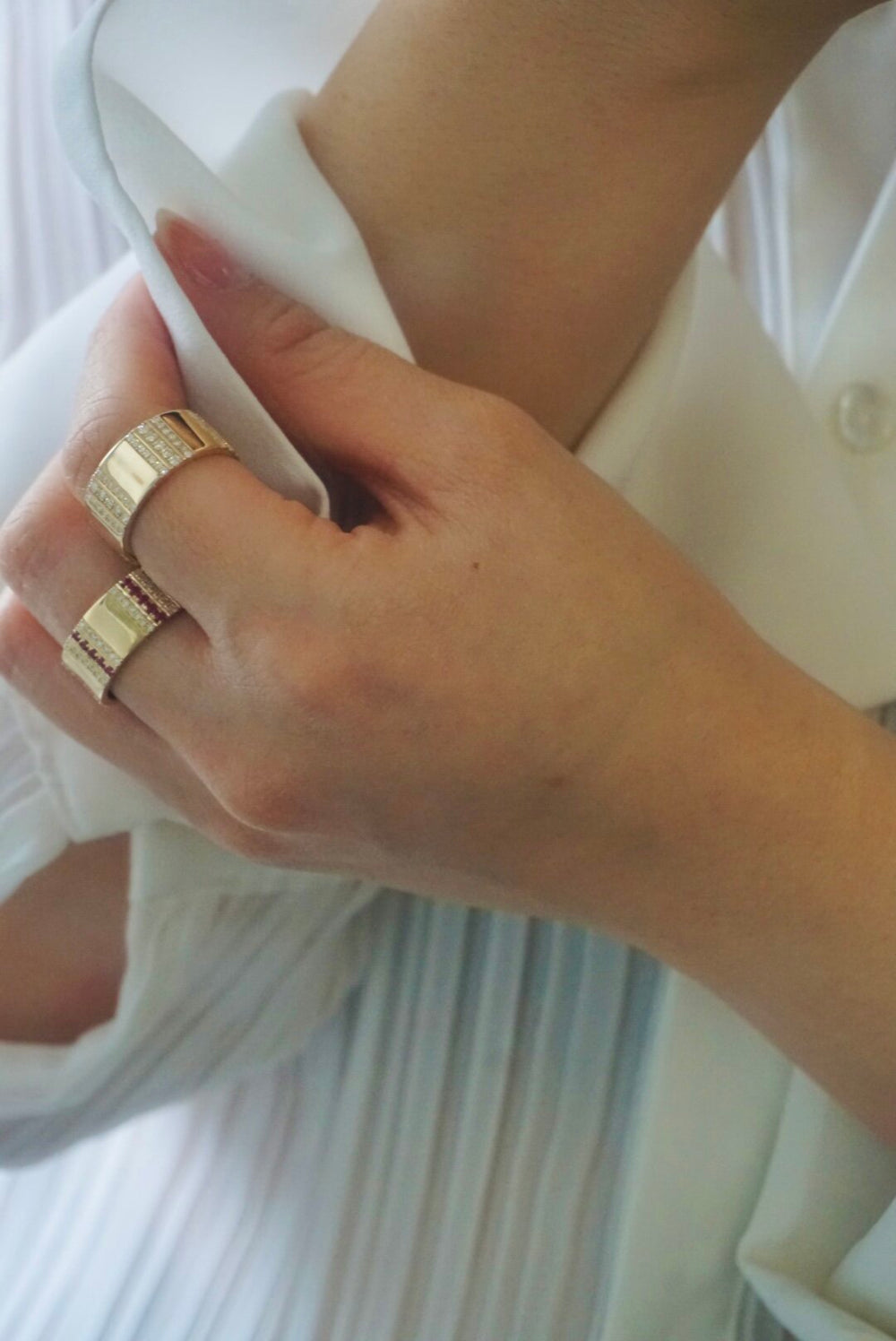 Close-up of Pinstripe Strength cigar band ring on hand showing pinstripe diamonds and rubies in yellow gold on white blouse