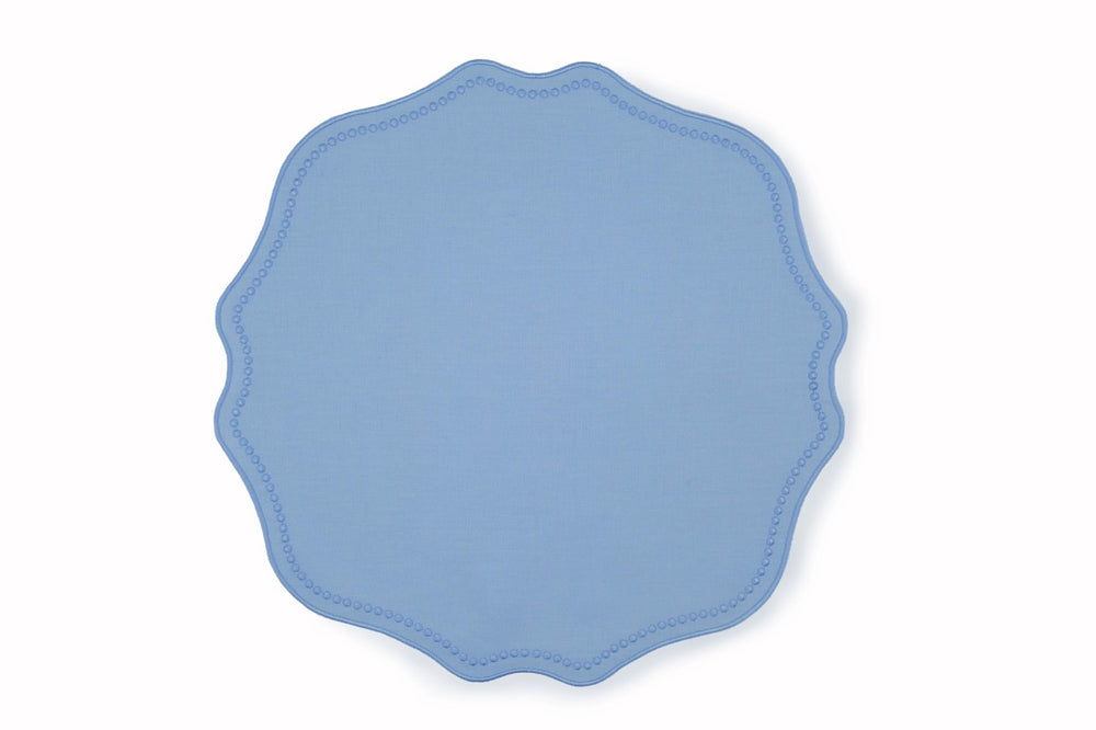 Top-down view of blue linen placemat with scalloped edge and dotted trim on white background