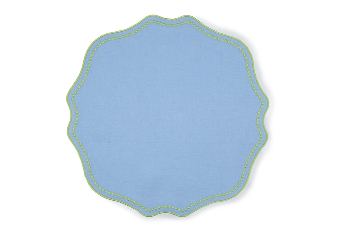 Top-down view of blue linen placemat with scalloped edge and lime green dotted trim on white background
