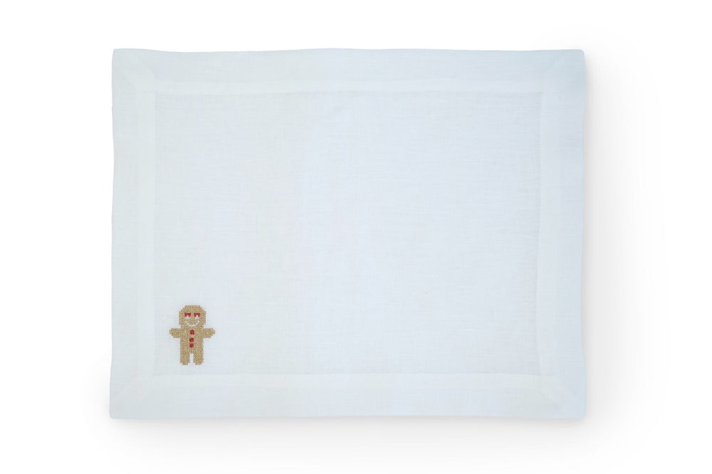 Top-down view of Sparkling Ginger Bread linen placemat showing small embroidered gingerbread man at lower-left and hemmed border