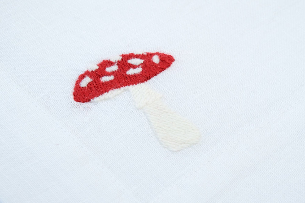 Close-up of white linen napkin showcasing red embroidered mushroom motif and fabric texture