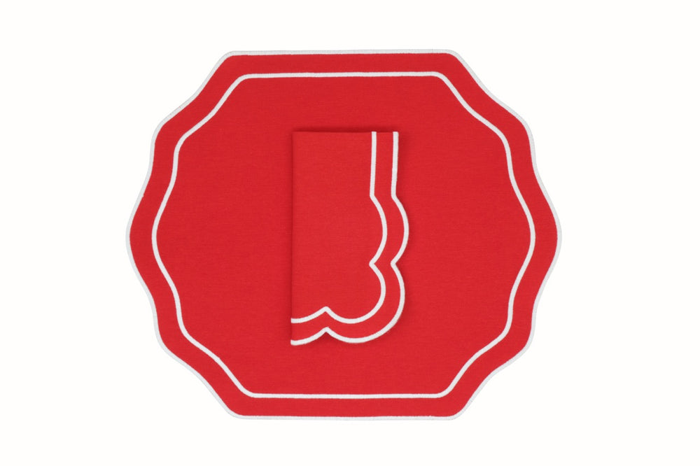Top-down view of stucco red napkin and placemat set showing scalloped white piped edging on a white background