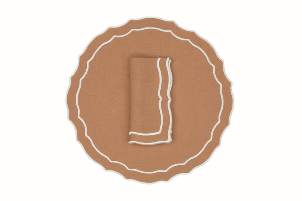 Top-down view of Vidro linen napkin and placemat set featuring tan fabric with white contrast scalloped trim on a white background