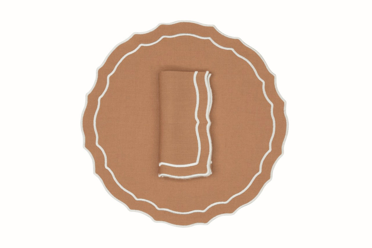 Top-down view of Vidro linen napkin and placemat set featuring tan fabric with white contrast scalloped trim on a white background