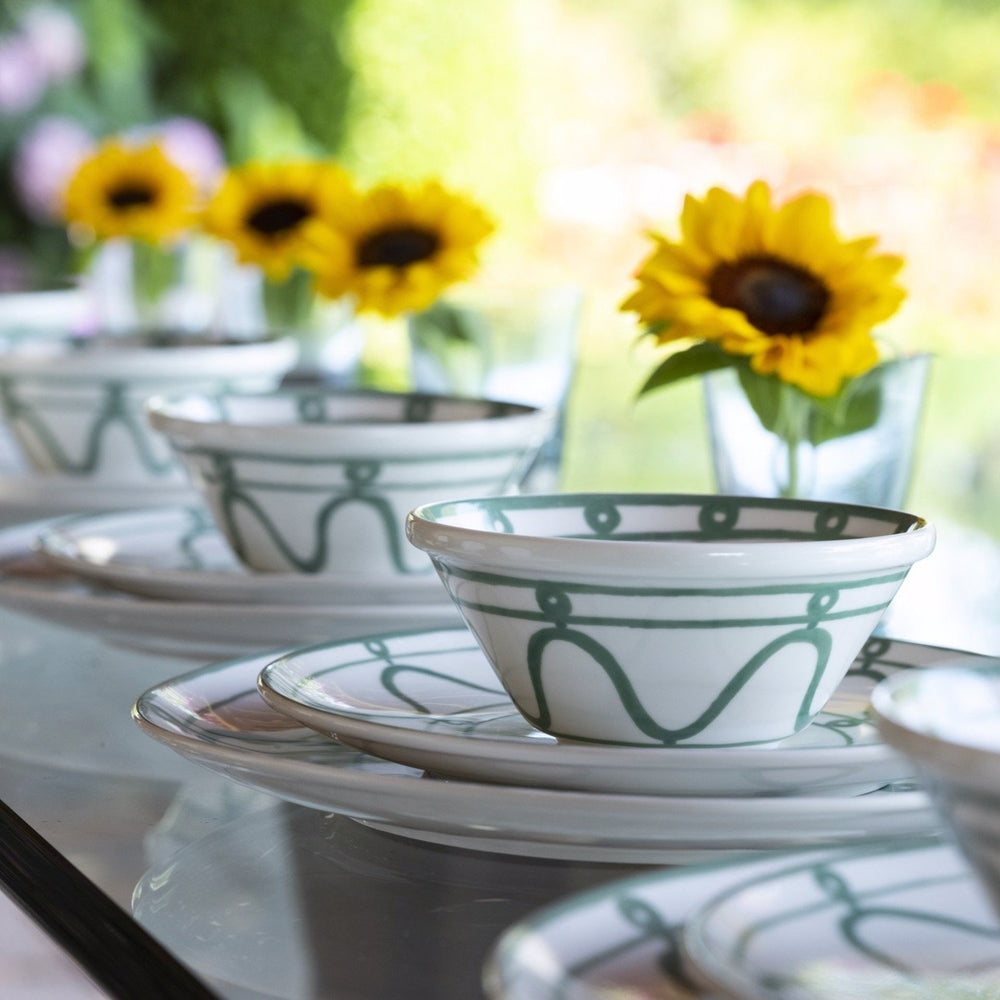 Front-right view of Serenity Bowl with green hand-painted geometric pattern on white porcelain, blurred sunflowers behind