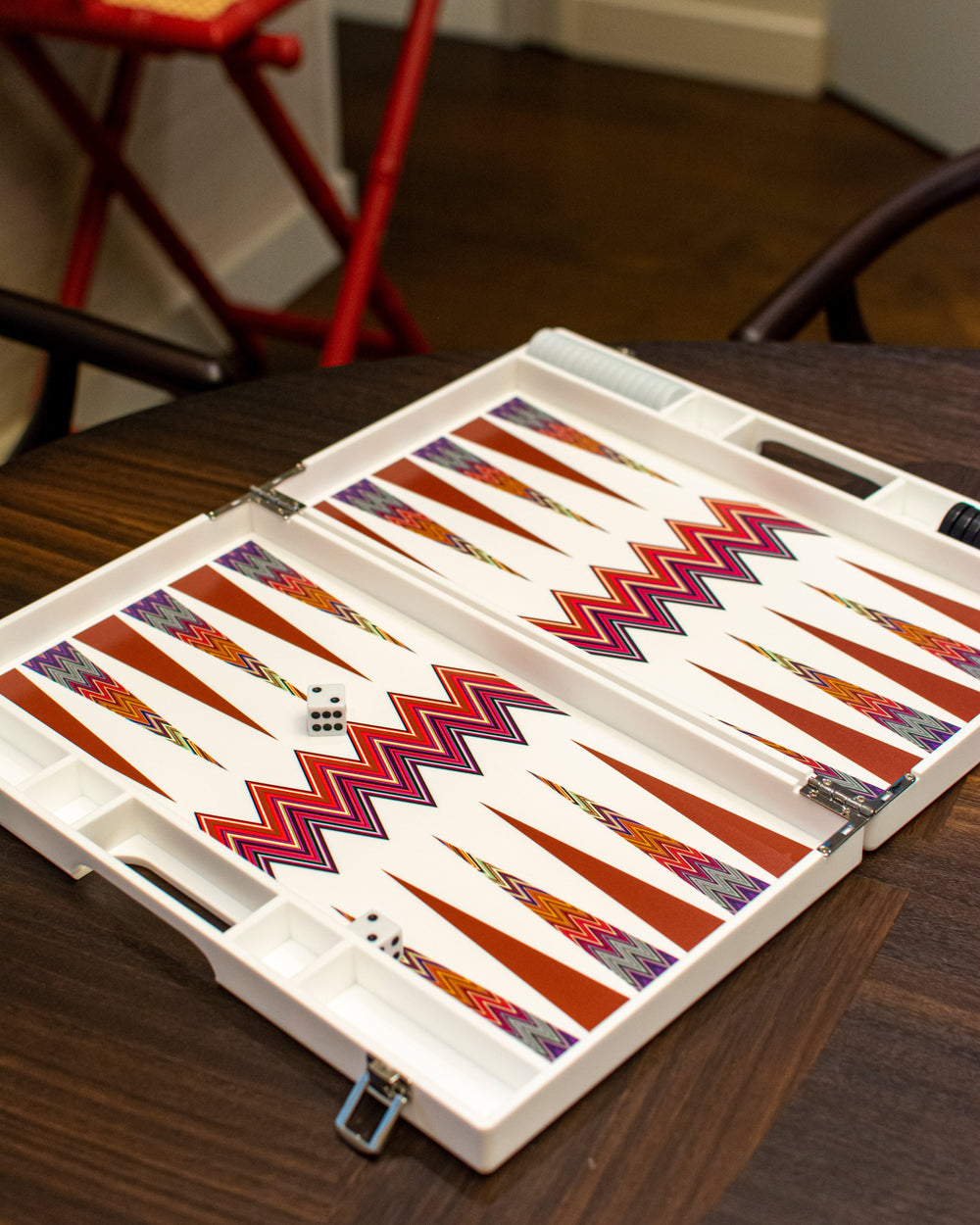 Angled view of Zig Zag backgammon board showcasing colorful zigzag points and white folding case with dice on a dark wood table