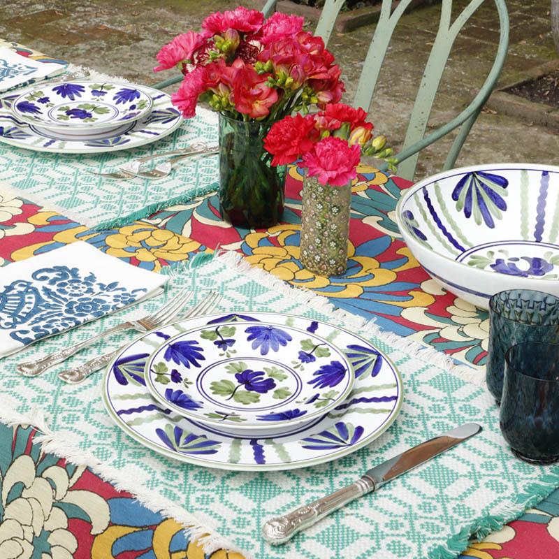 Angled view of Blossom Dessert Plate Blue showcasing floral motifs inspired by Italian ceramics on a patterned table